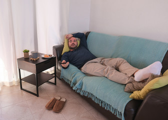 Young man is bored on the couch at home and watches TV - Home isolated  because of the coronavirus...