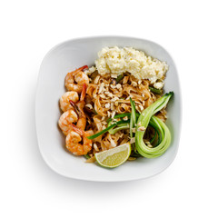 Fried udon noodles in a wok with shrimp and nuts. Served with fresh cucumber and lime. Traditional asian food. Isolated on a white background.