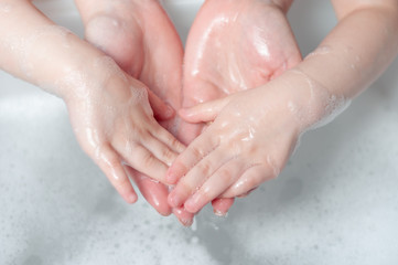 Mom washes hands with soap to her baby. Teaches a child how to wash hands with soap.