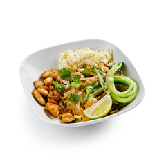 Fried udon noodles in a wok with pieces of pork. Served with tofu cheese, fresh cucumber and lime. Traditional asian food. Isolated on a white background.