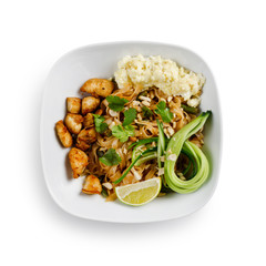 Fried udon noodles in a wok with pieces of pork. Served with tofu cheese, fresh cucumber and lime. Traditional asian food. Isolated on a white background.