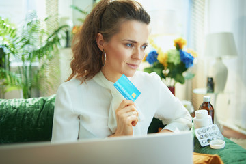 pensive stylish woman with laptop, credit card and pills