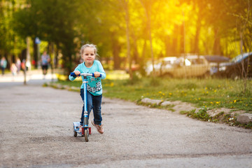 Little beautiful girl on a walk rides a scooter