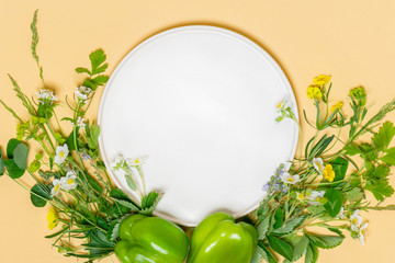 Natural healthy food concept. Meadow grass and wild flowers around an empty white plate on a light beige background, top view, copy space. Summer food, organic cuisine.
