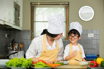 Happy  Asian  mother  with  son in chef  hat  cooking  salad in kitchen at home