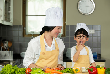 Happy  Asian  mother  with  son in chef  hat  cooking  salad in kitchen at home