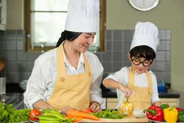 Happy  Asian  mother  with  son in chef  hat  cooking  salad in kitchen at home