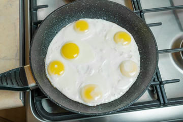 Six eggs in close-up frying in a pan on a gas stove, top view