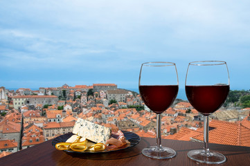 Two glasses of red wine with charcuterie assortment on view of Dubrovnik red roofs. Glass of red wine with different snacks - plate with ham, sliced, blue cheese. Couple romantic celebration.