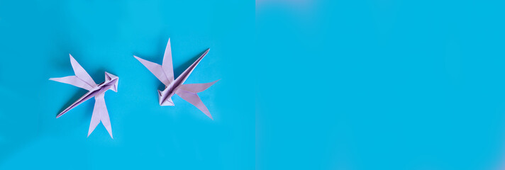 Origami two violet dragonfly on a blue isolated background. board, World Peace Day concept. Close up studio photo. child made bird.craft, hobby and creativity concept