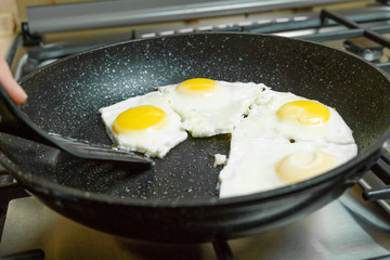 woman's hand using a black spatula takes a fried egg from the pan