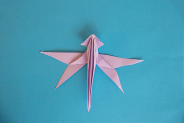 Origami violet dragonfly on a blue isolated background. board, World Peace Day concept. Close up studio photo. child made bird.craft, hobby and creativity concept