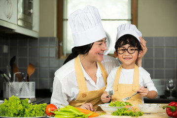 Happy  Asian  mother  with  son in chef  hat  cooking  salad in kitchen at home