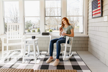 Mom holding her newborn baby sitting in screened porch. Military mom with a baby in her sun room.