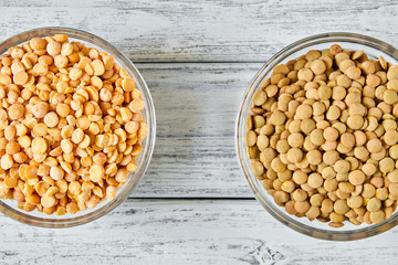 Raw yellow dry peas and lentil grains in a transparent glass plate on wooden background. Problem of choice. Closeup, top view