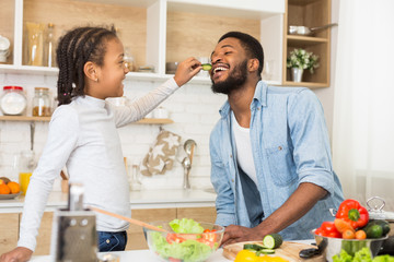 Cute little girl feeding her daddy while cooking