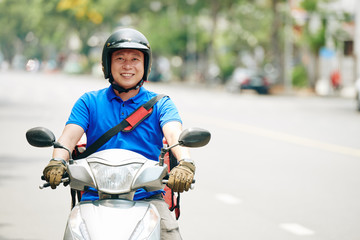 Smiling Asian delivery man riding scooter in the city and delivering products