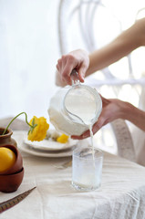 The girl's hands pour milk from a glass jug into a glass. Serving in rustic style. An organic Breakfast. Rustic style. Simplicity.