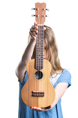 Teenage, blond girl in blue T-shirt is holding light brown ukulele instrument.