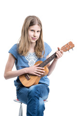 Teenage, blond girl in blue T-shirt is sitting and playing music on ukulele instrument.