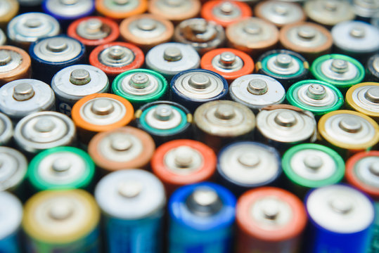 Close up of positive ends of colorful discharged batteries of different sizes and formats, top view, copy space. Used alkaline battery on concrete background. Hazardous garbage concept.
