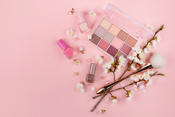 Makeup cosmetics and cherry blossoms on a pink background. Close-up with space for text.