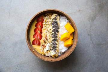 Mango smoothie bowl with strawberry, banana,coconut and oatmeal on concrete background.