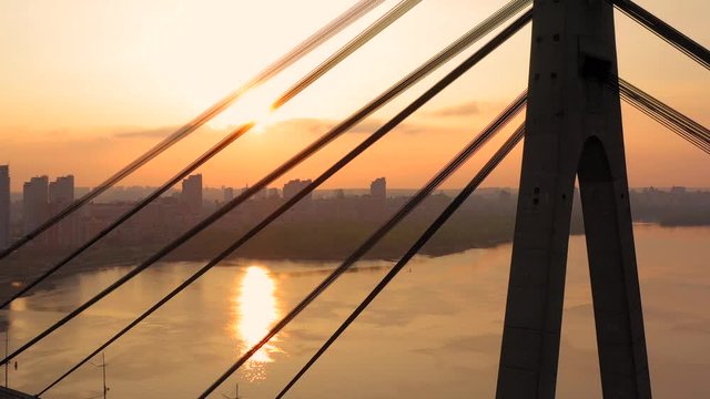 Aerial drone view View Of North or Moscow Bridge Kiev, Ukraine over Dnieper. Drone span between the cables of the bridge. Sunset sun. City view. Rays of the sun through the cables of the bridge