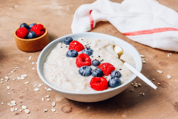Breakfast oatmeal porridge with fresh berries and almond milk. Healthy vegan food concept. Beige rustic background. Selective focus