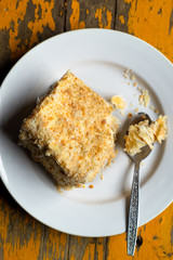 Homemade mille-feuille, puff pastry custard cream pie on white plate on old yellow painted wooden background, top view