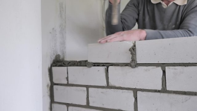 builder hands, the man puts the bricks on concrete. Male builder laying white brick on cement and standing wall. Hands of a man laying building bricks 