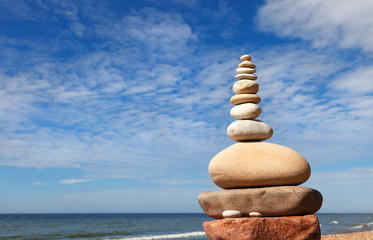 Rock zen pyramid of white and pink pebbles on a background of blue sky and sea.