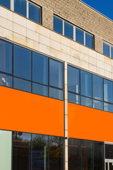 The orange plate on the wall. Blank plate on a building wall with glass windows.