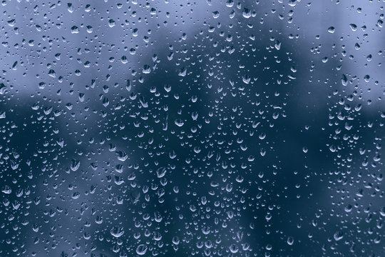 big rainy droplets on a blue black glass window surface. water drops on dripped background pane in a rainy days in night city. stormy weather. isolation sad depression concept. rainy season.