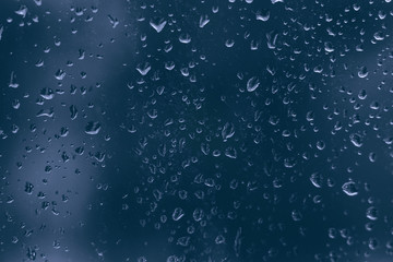 rainy droplets on a dark blue glass window car surface. water drops on transparent background shield in a rainy days in night city . stormy weather. isolation sad depression concept. rainy season.