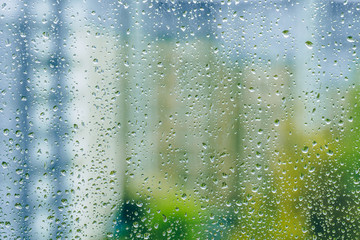 rainy droplets on a wet window glass transparent surface. drops on window pane in a rainy days in the city. stormy weather. isolation sad depression concept. rainy season. buildings houses.