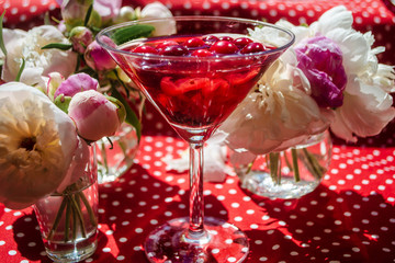 Magic solemn still life with glass of red drink with autumn organic berries surrounded by white flowers in the diagonal striped shadow of the blinds on a bright sunny day. Greeting card on textile