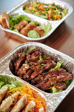 Foil tray with delicious ready meal of grilled barbecued pork ribs with sweet sauce and fresh salad