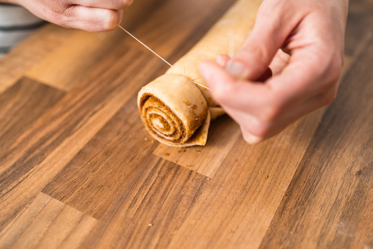 Woman's hands cutting dough with yarn to prepare homemade cinnamon rolls.