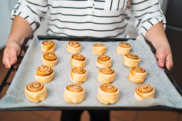 Close up of a woman with a tray of raw homemade cinnamon rolls ready to bake.
