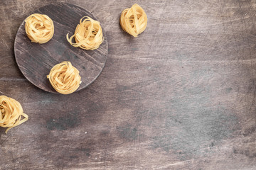 Italian pasta nest on dark brown plywood table. Mediterranean cuisine cover