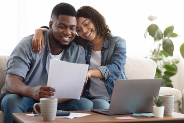 Family insurance. Black couple reading documentation at home, checking agreement together