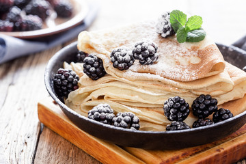 Pan of crepes with fresh blackberries on wooden table