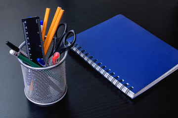 Stand with office supplies and blue notebook on black wooden table