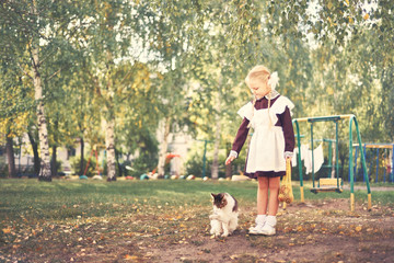 little girl schoolgirl in uniform plays in the yard with homeless cat.