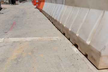 Long view down a row of hard plastic orange and white traffic barriers beside a road construction site, horizontal aspect