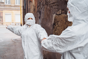 Woman medic in a protective suit and medical mask pulling doctor to save lives. They are scared, but ready to help people. Woman showing the direction where to go. Coronavirus concept. Covid-19