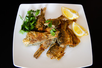 Fried fish on a white plate. Grilled crucian with lemon and parsley.