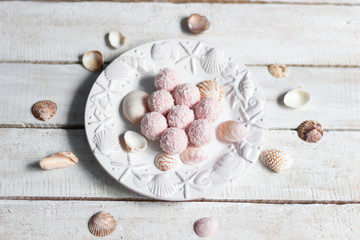 Fototapeta na wymiar Pink raspberry sweet energy balls with coconut flakes in bowl with sea shells on white wooden background