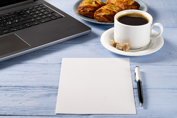 Obraz na płótnie Canvas Laptop with cup of coffee and bakery on light blue old wooden table. Notebook with cup of fresh coffee in home office. Working from home concept